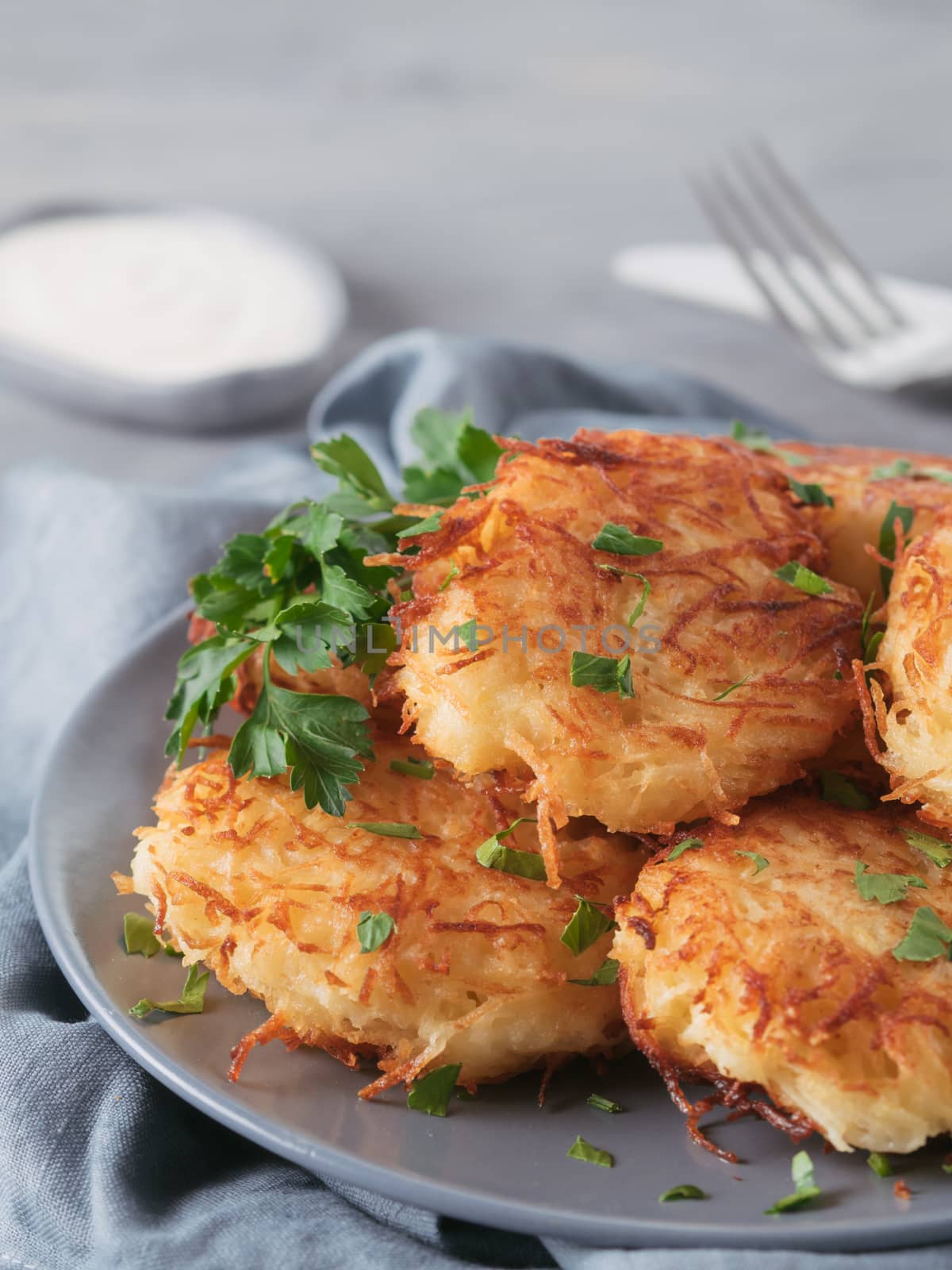 Close up view of potato pancakes. Potato flapjack on gray plate over gray wooden table, with fresh parsley and sour cream. Copy space for text. Vertical.