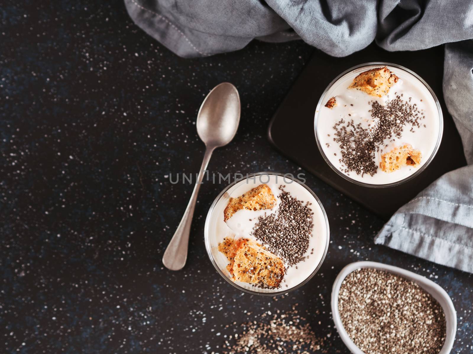 No baked cheesecake dessert with crushed carrots biscuits and chia seeds in glass jar on dark background. Ideas and recipes for healthy breakfast. Copy space for text. Top view or flat-lay.