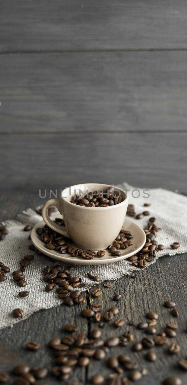 Coffee cup filled of fresh arabica or robusta coffee beans with scattered coffee beans on a linen textile and wood table