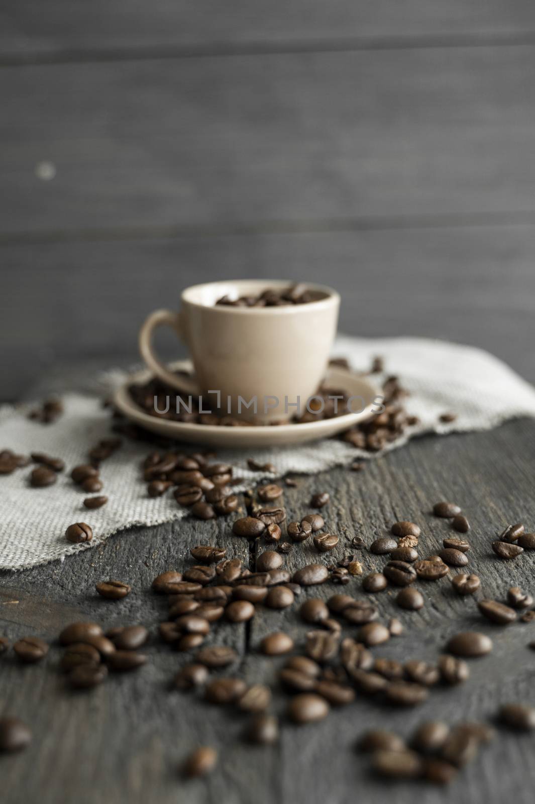 Coffee cup filled of fresh arabica or robusta coffee beans with scattered coffee beans on a linen textile and wood table