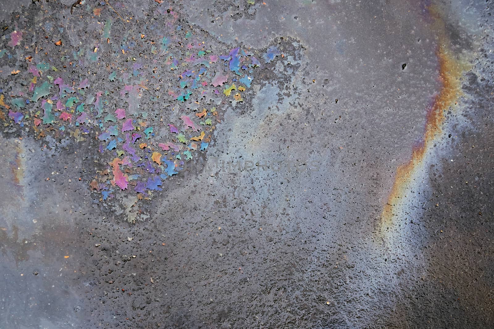 Gas stain on wet asphalt caused by a leak under a car or truck, abstract background