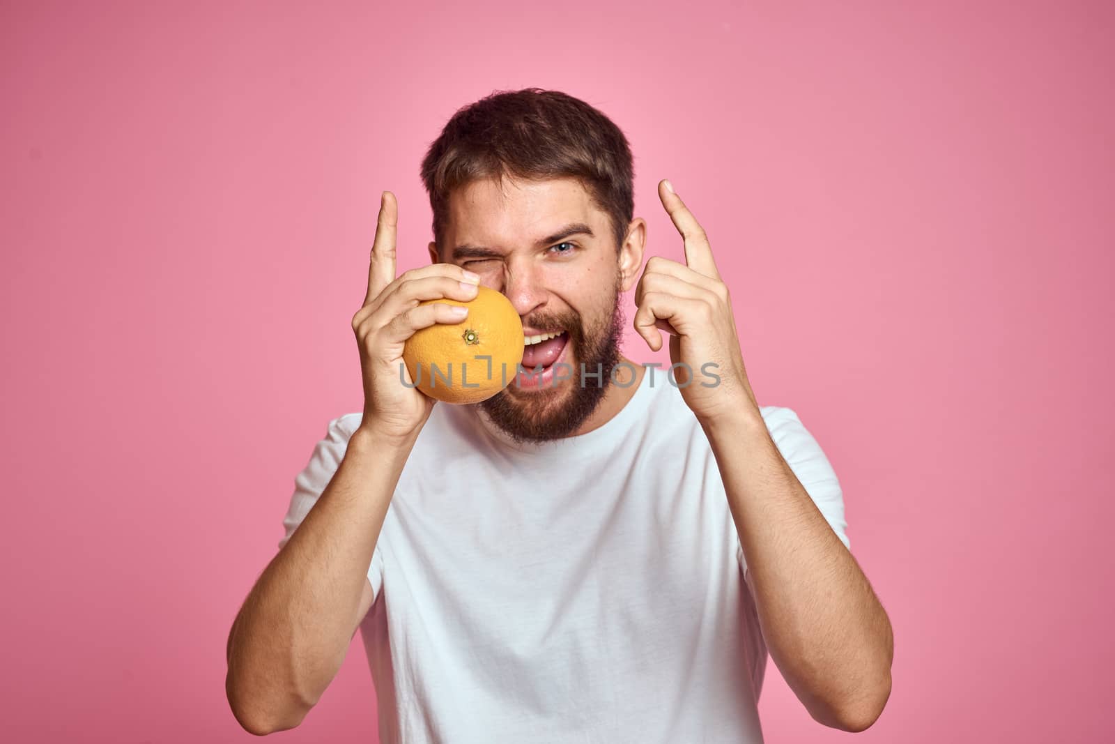 Young man with orange on a pink background in a white t-shirt emotions fun gesticulating with model hands. High quality photo