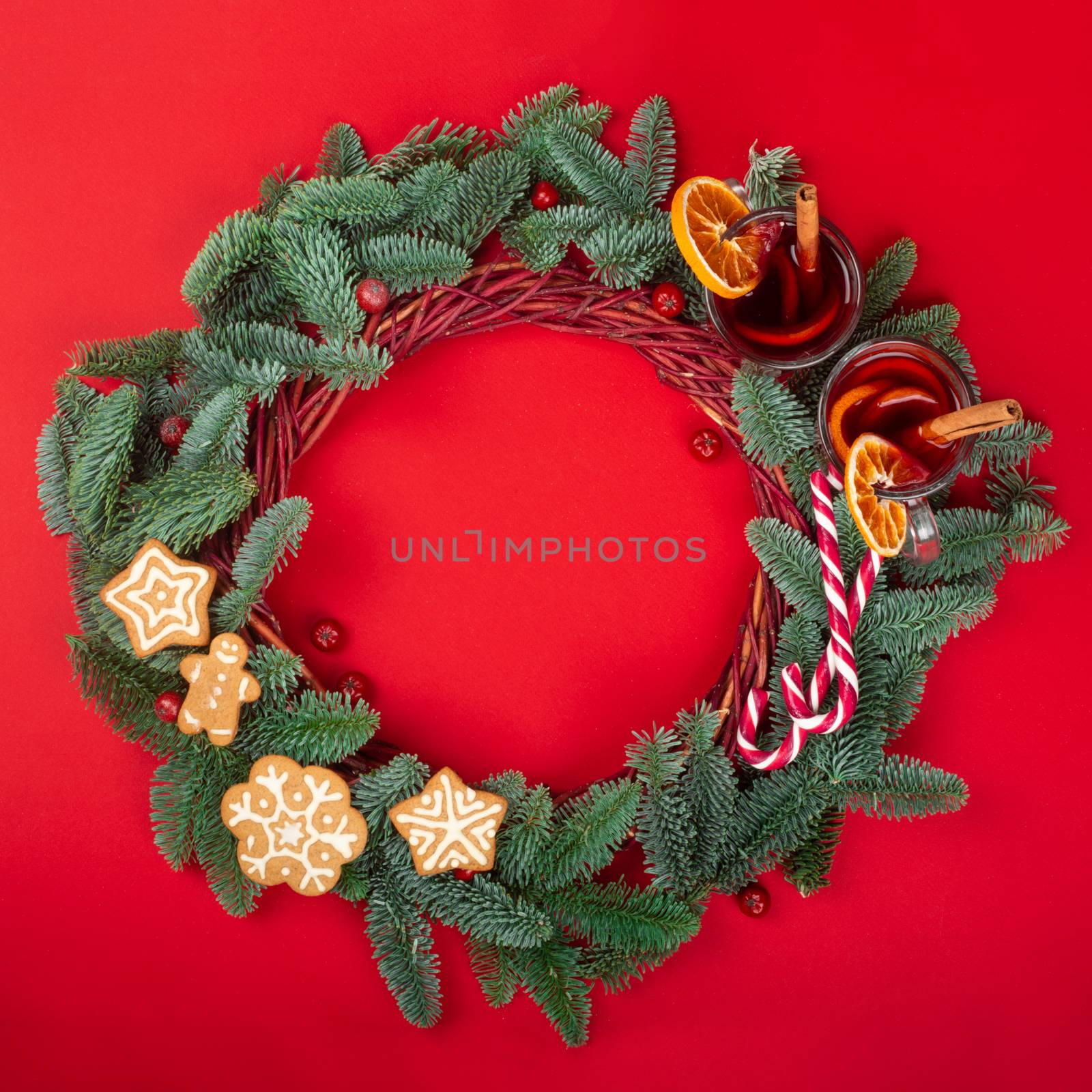 Christmas decorative wreath with noble fir tree twigs pine cones mulled wine and gingerbread cookies on red paper background with copy space for text