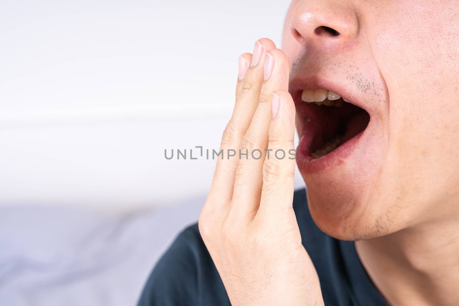 Asian man are yawning covering open mouth with hand after he wake up. Healthcare medical or daily life concept. by mikesaran