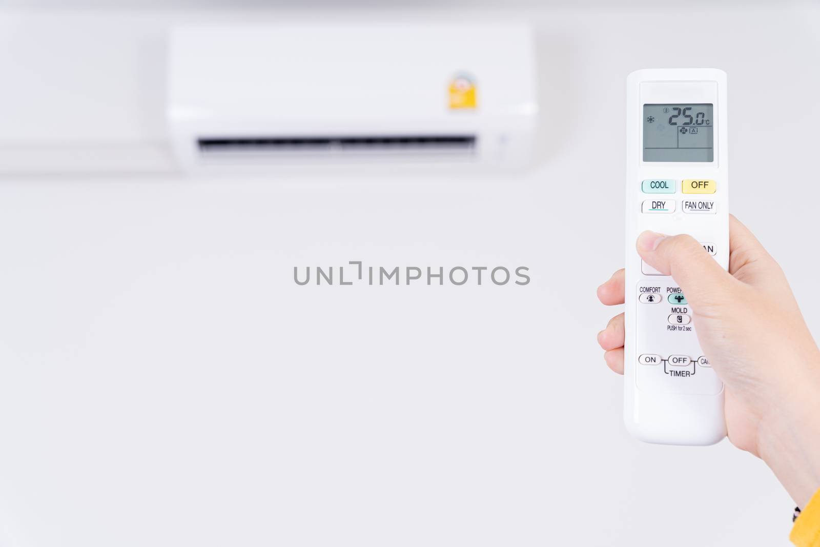 Human hand is using white remote of air conditioner for turn on or adjust temperature of air conditioner inside the room.