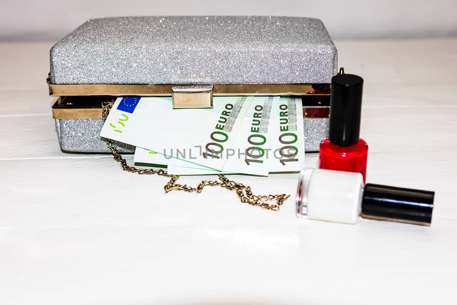 Glittery silver clutch bag with money and beauty products isolated on white background with copy space.