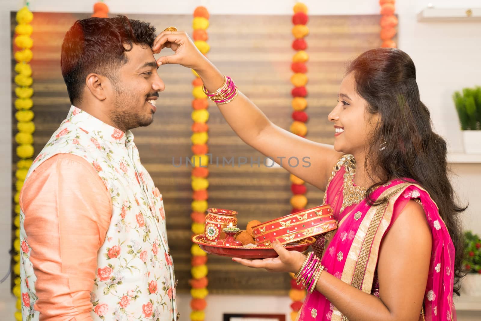 Woman applying Thilaka or Mark to his partner or husband's forehead during Karwa Chauth festival celebration while both in traditional dress. by lakshmiprasad.maski@gmai.com