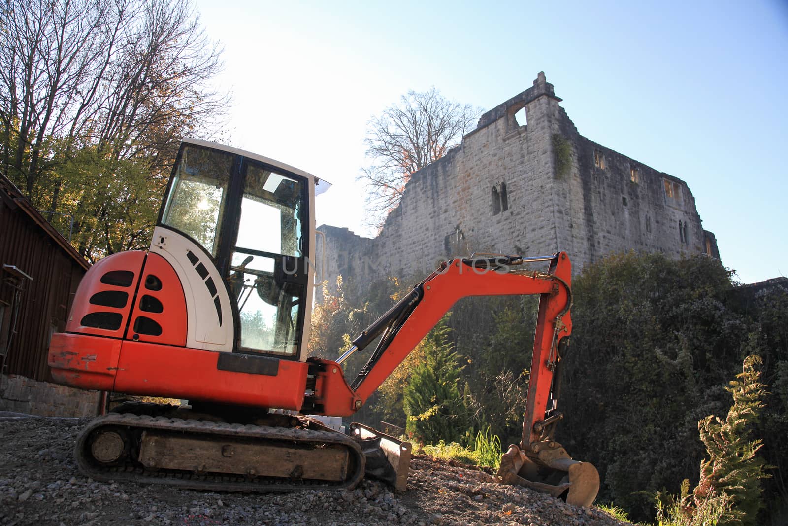 Small excavator on a consruction site hill in front of an ancient castle ruin