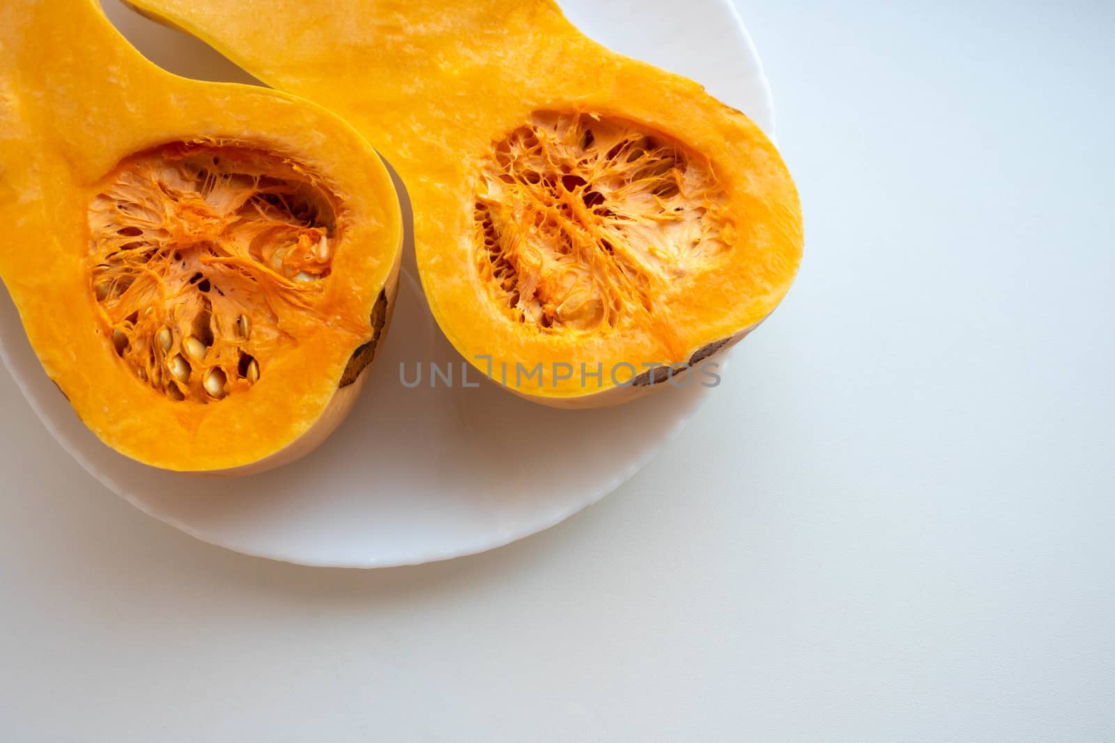 Two orange pumpkin halves on a plate on a white background. The concept of Halloween ,harvest,thanksgiving,vegetarianism by lapushka62