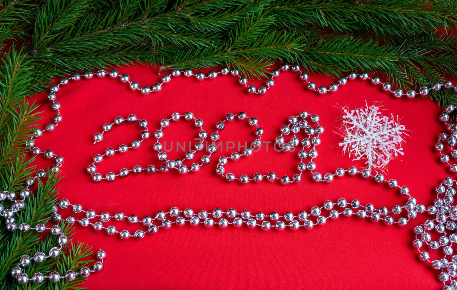 Spruce branches on a red background and numbers 2021 ,lined with silver beads. The concept of a new year.