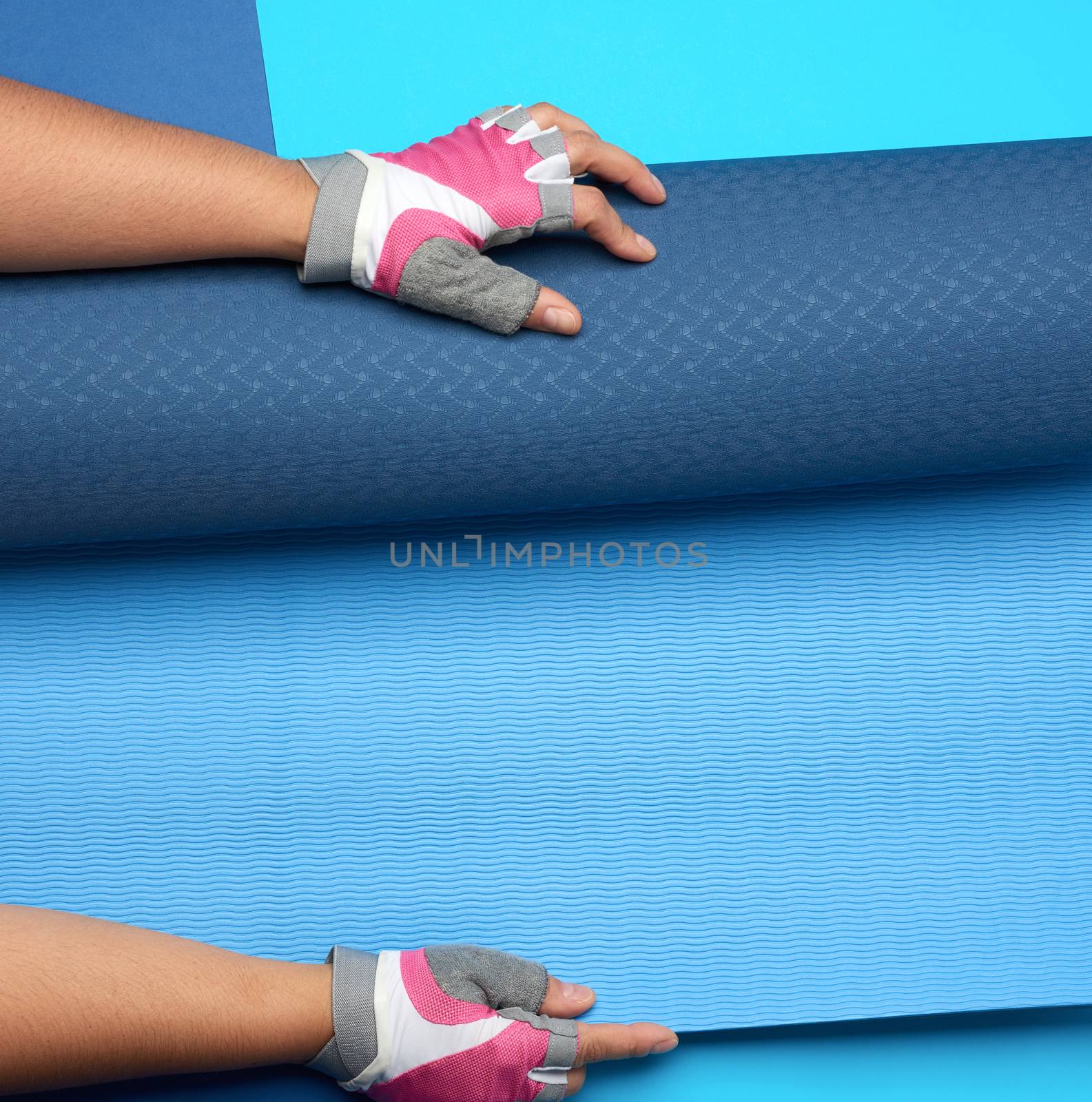 female hand holds a rolled up neoprene sports mat on a blue background, top view