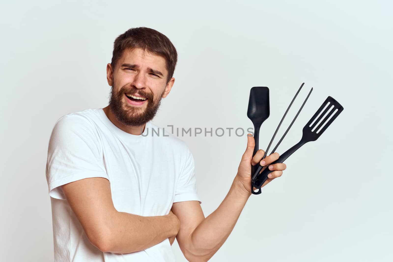 A man with kitchen appliances in the hands of their white T-shirt on a light background cropped view. High quality photo