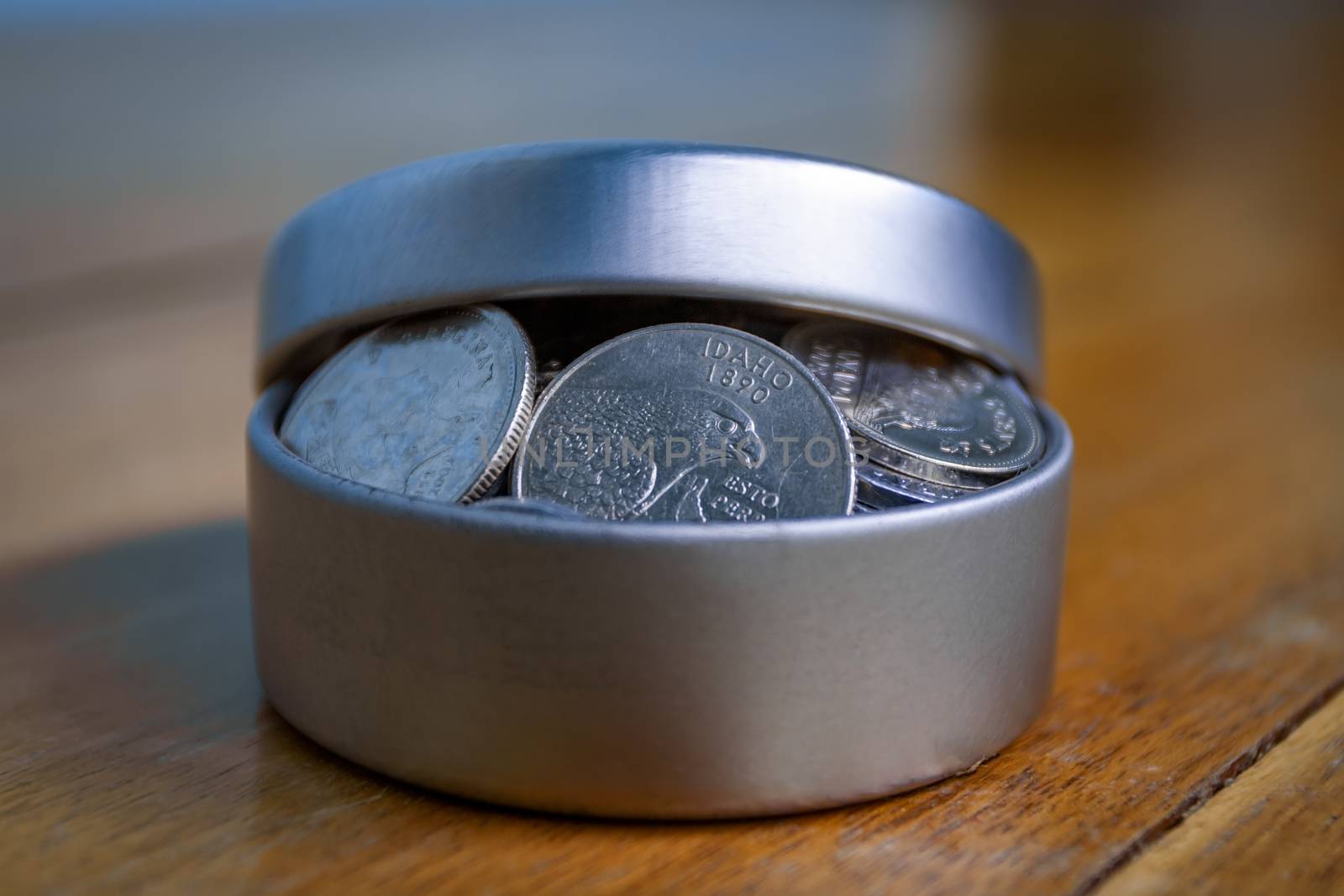 Open silver container filled with coins on a wooden table and an unfocused background