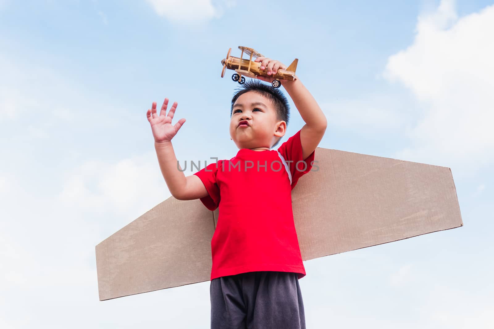 Happy Asian funny child or kid little boy smile wear pilot hat play and goggles with toy cardboard airplane wing flying hold plane toy outdoor against summer blue sky cloud background, Startup freedom
