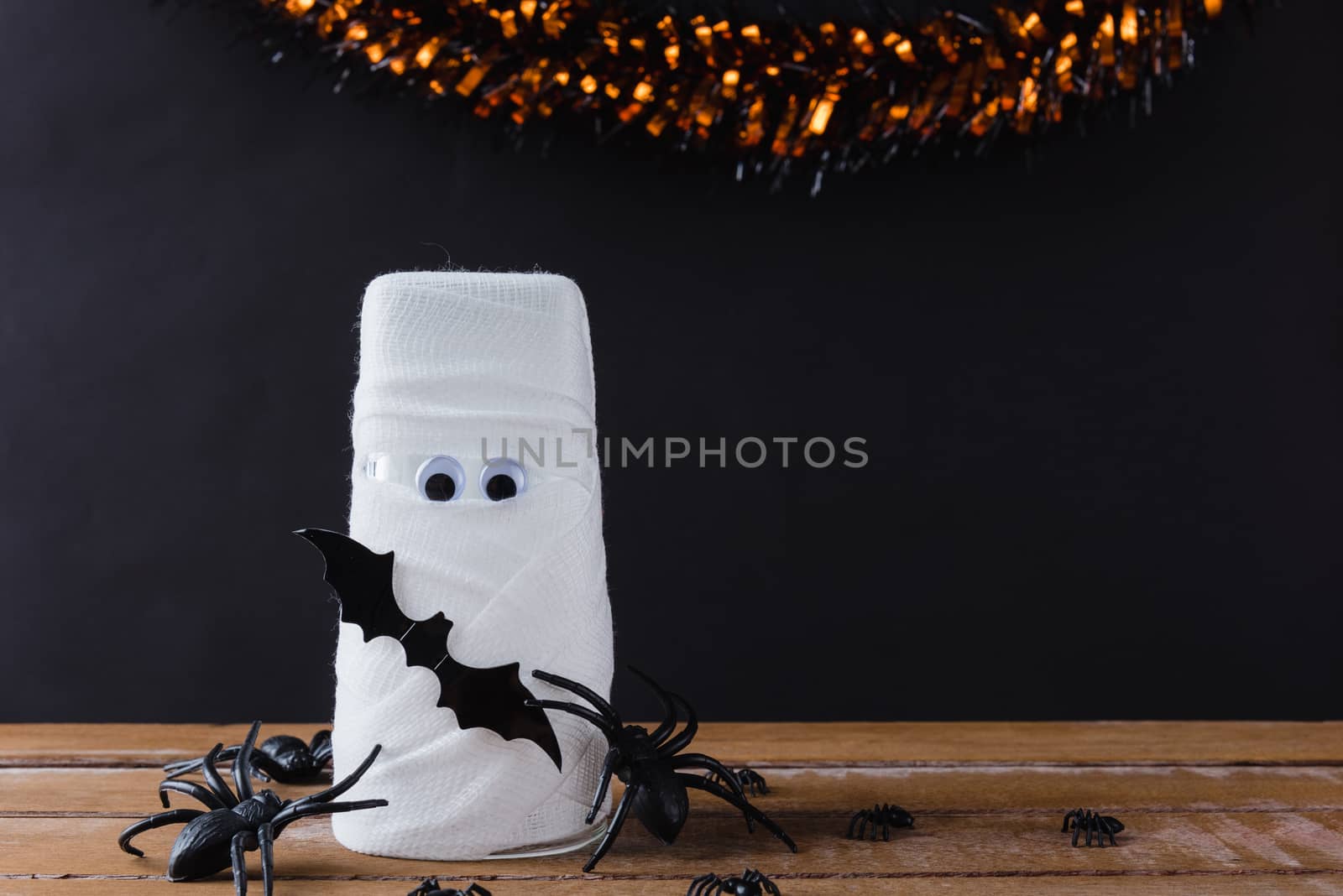 Funny Halloween day decor party concept, The mummy ghost on water glass wrapped around with bandage and have bats and spider stick it found only eyes, studio shot isolated on black background