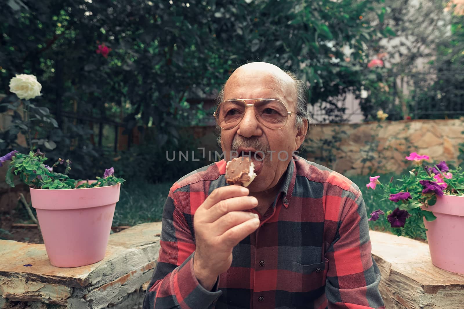 Elderly man eating ice cream on stick in the backyard.