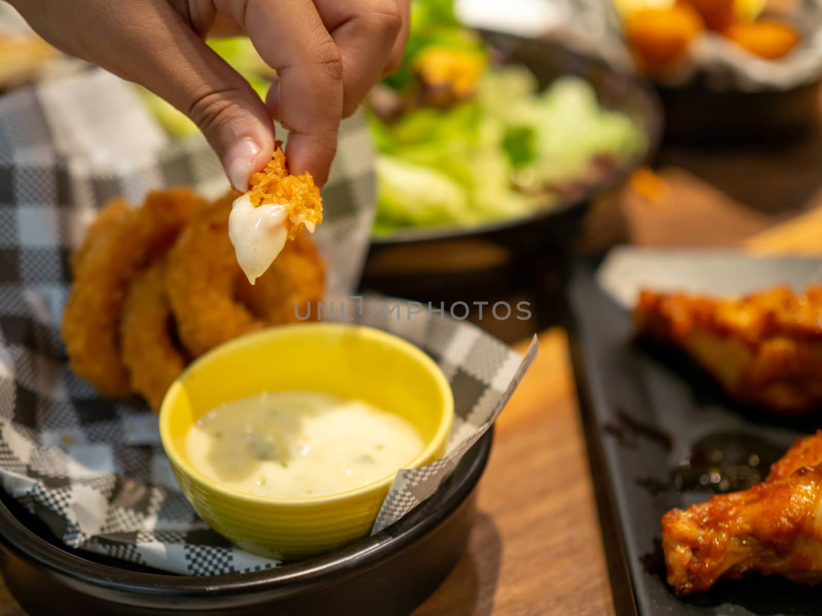 Human hand holding fish finger and dipping on mayonnaise sauce with blurry background.Healthy food or snack for children concept.