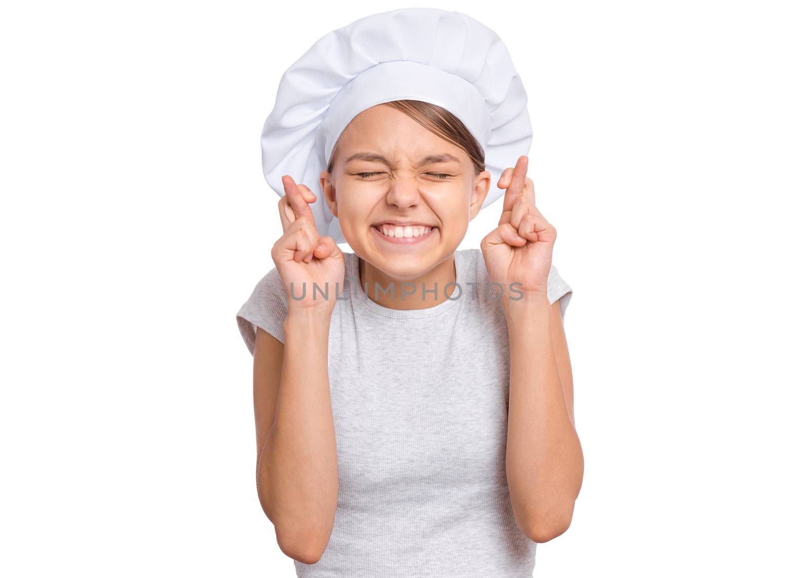 Teen girl in chef hat, keeping fingers crossed and making wish, isolated on white background.