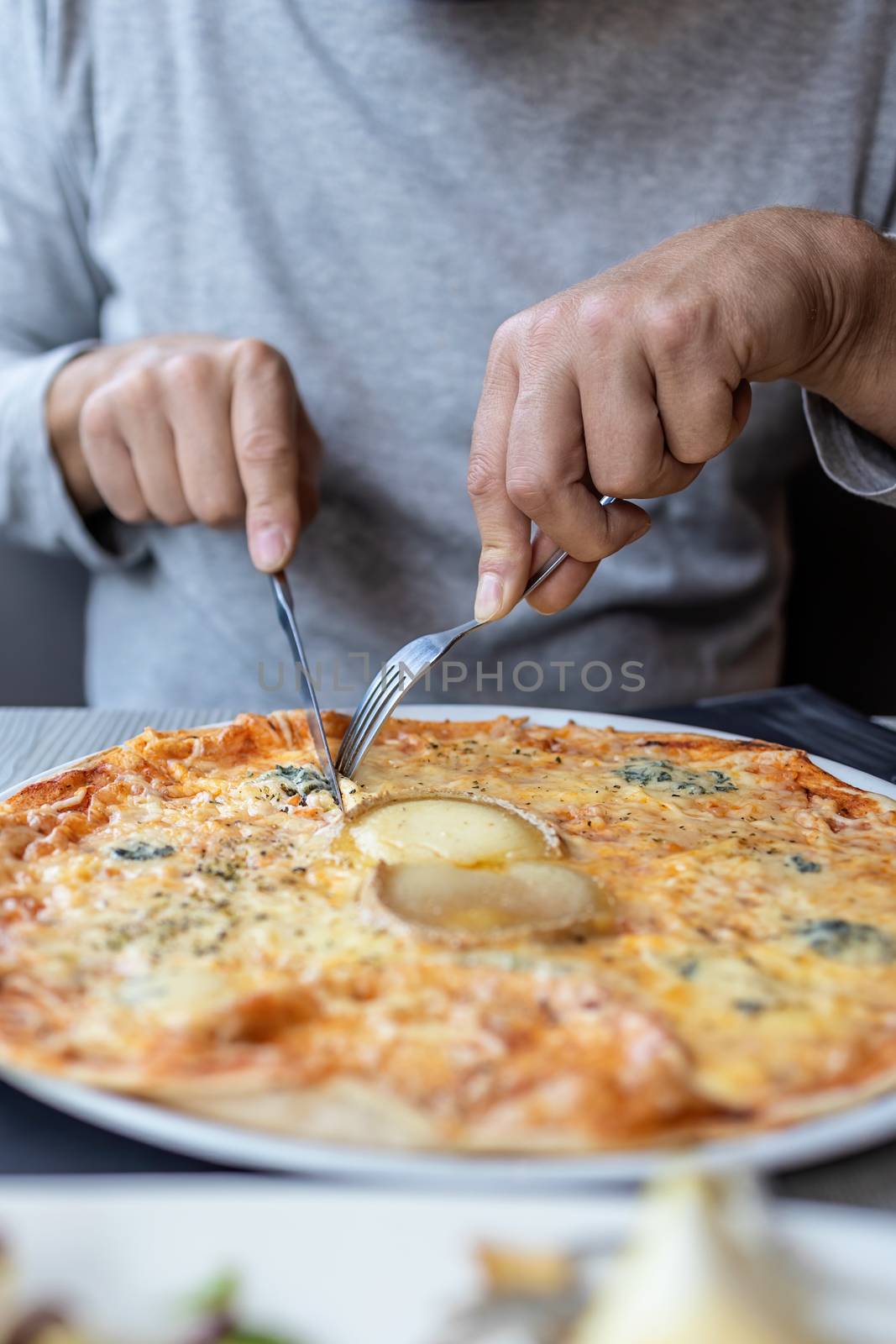 Man eating delicious cheesy pizza in the restaurant with fork and knife by Digoarpi