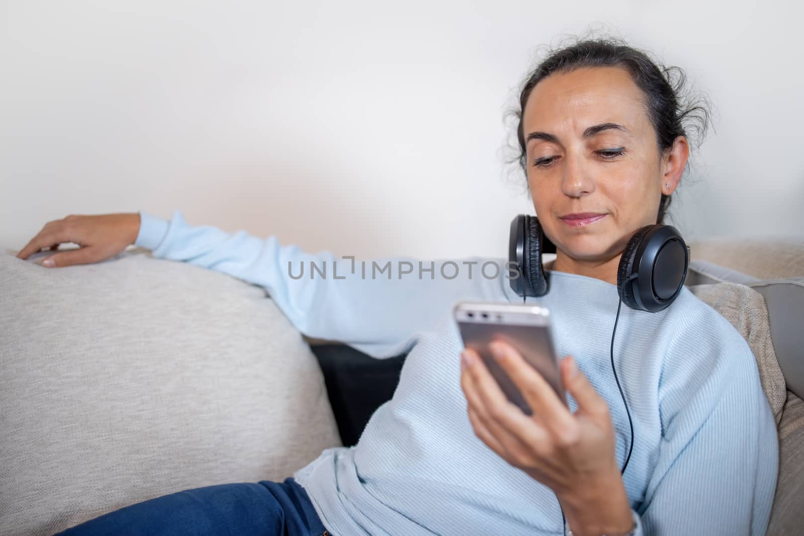 Pretty girl at home on the couch with headphones using smartphone
