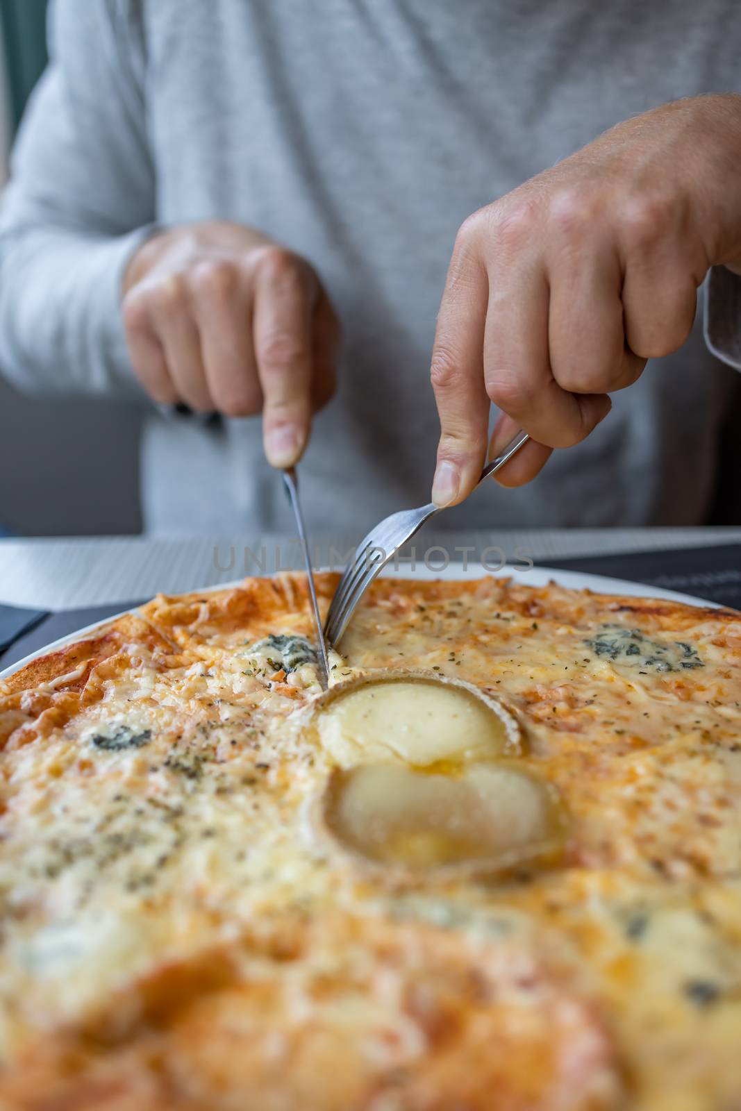 Man's hands cut a piece of cheesy pizza in the restaurant