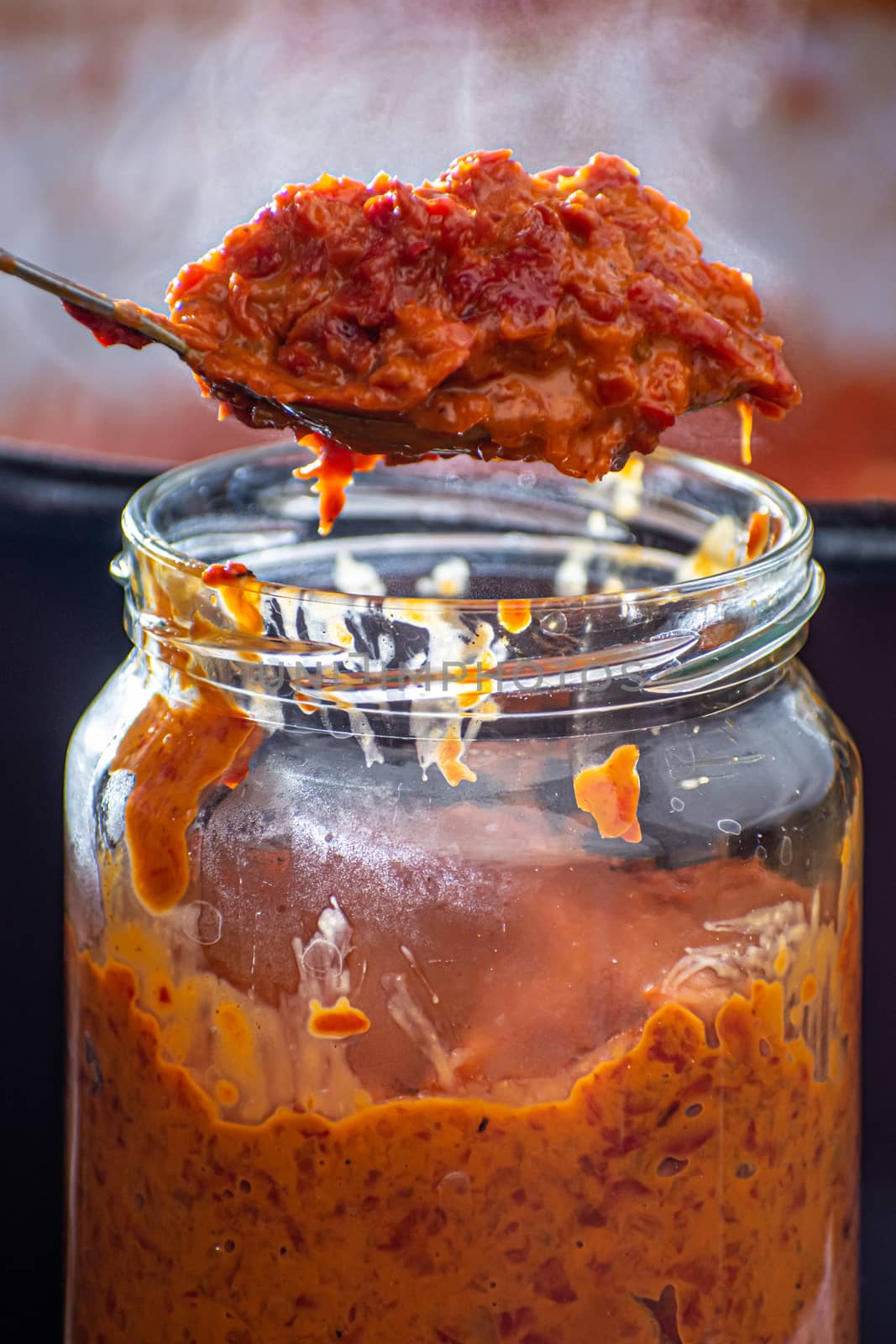 pouring fresly cooked ajvar into the jar with spoon