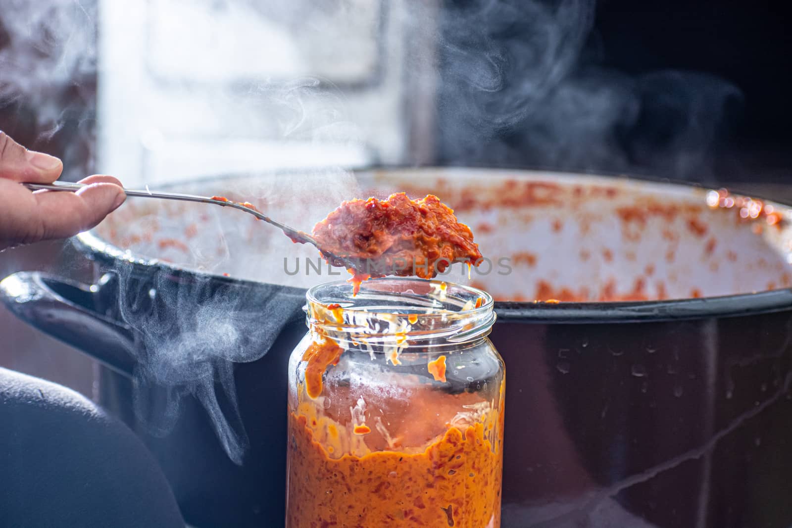 pouring fresly cooked ajvar into the jar with spoon