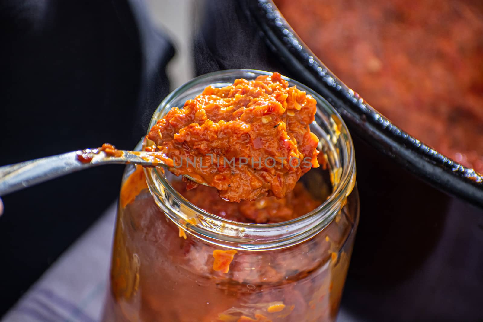 pouring fresly cooked ajvar into the jar with spoon