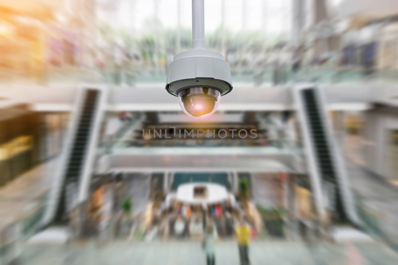 Closeup CCTV security camera on blurred inside shopping mall background.