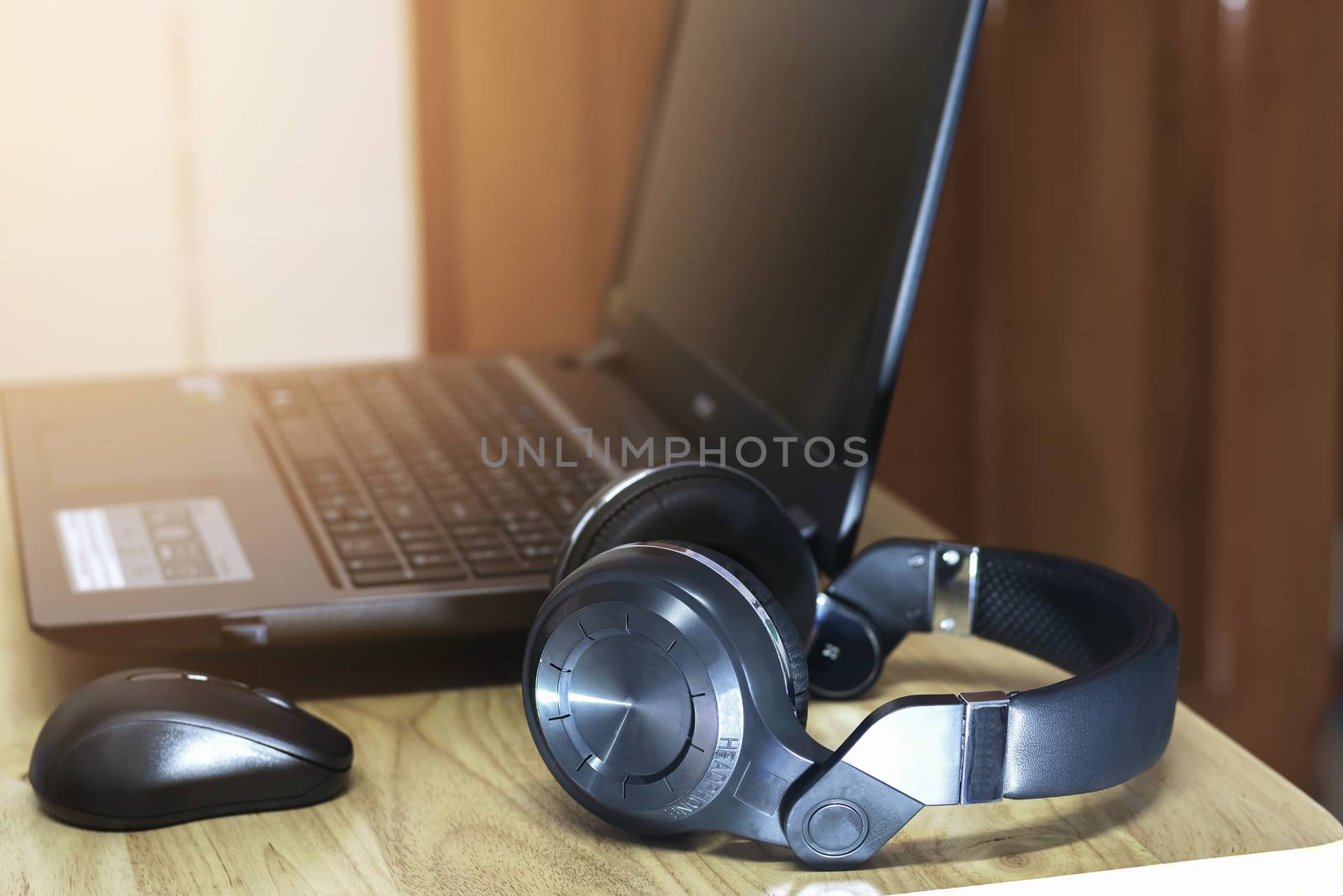 Closeup a headphone on the wooden table with a wireless mouse and computer notebook.