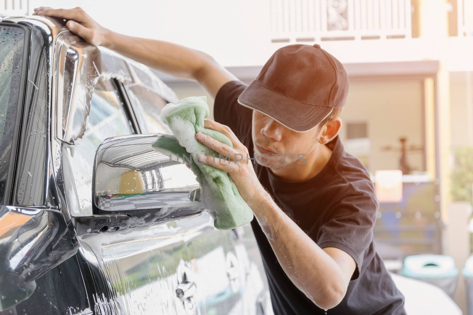 Car wash worker wearing a T-shirt and a black cap is using a sponge to clean the car in the car wash center, concept for car care industry.