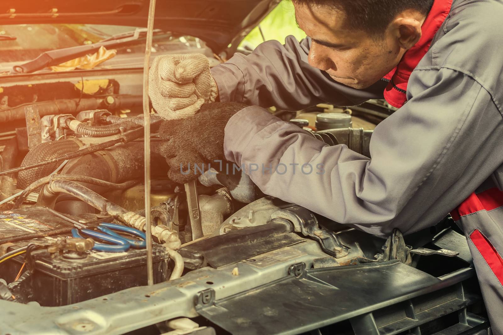 Car mechanic in grey uniform are using a wrench nut at the engine of the car for maintenance, Automotive industry and garage concepts.