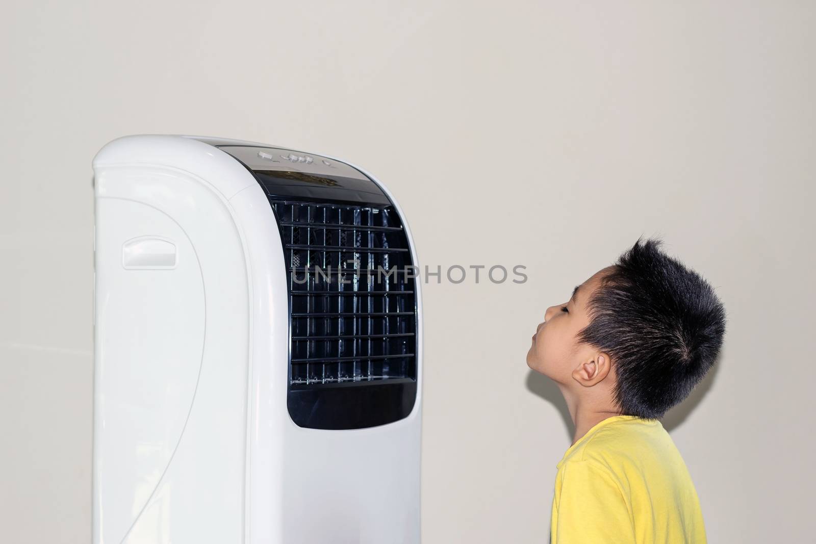 Because of the hot weather, the boy stood by the fan blowing cold air to his face.