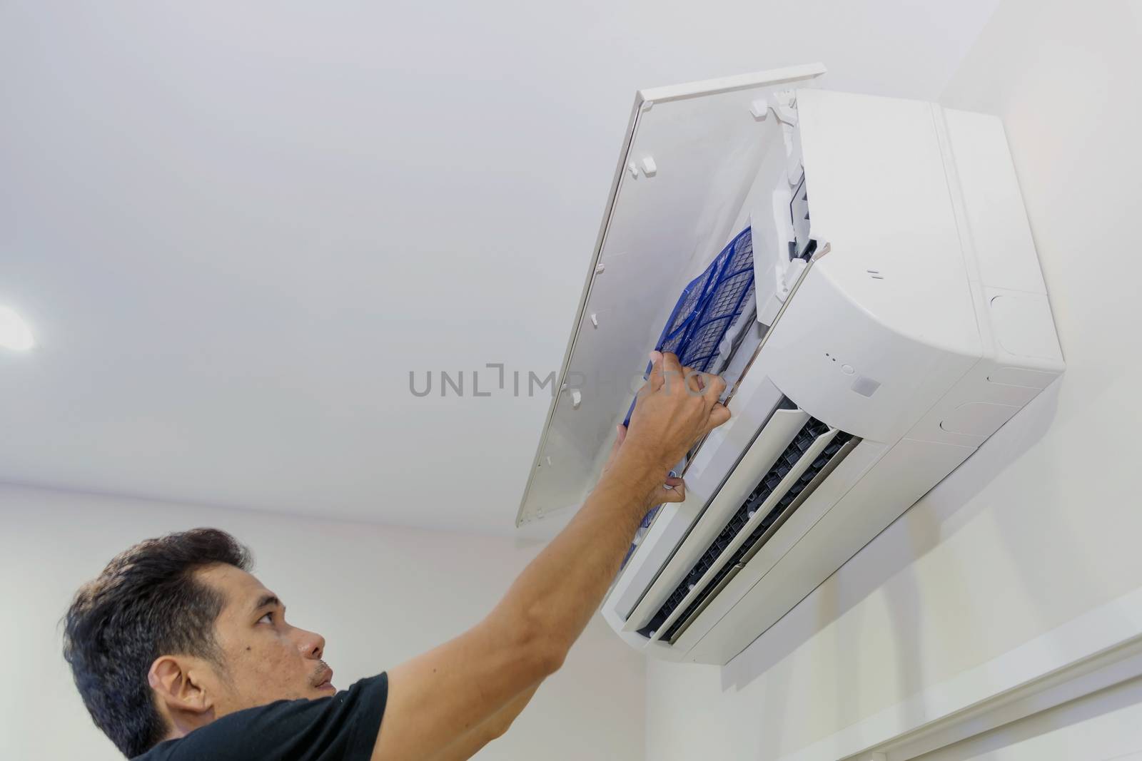 A man is removing the air filter of the air conditioner for cleaning.