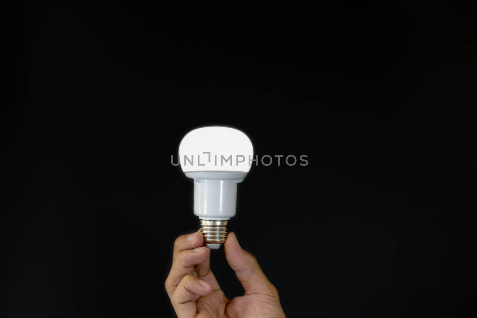 Hand holding LED light bulb over black background.