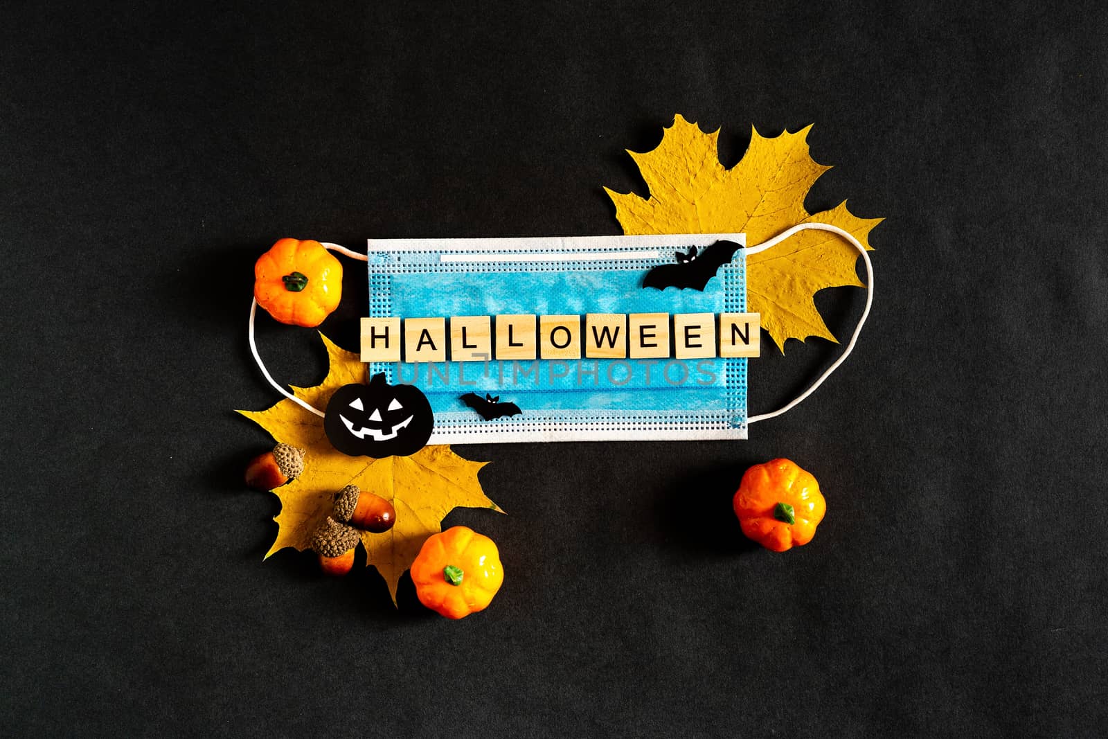Halloween pumpkins, protective medical mask and yellow maple leaves on a black background, bats made of black paper. The inscription HALLOWEEN The concept of Halloween and covid-19. Flatlay.