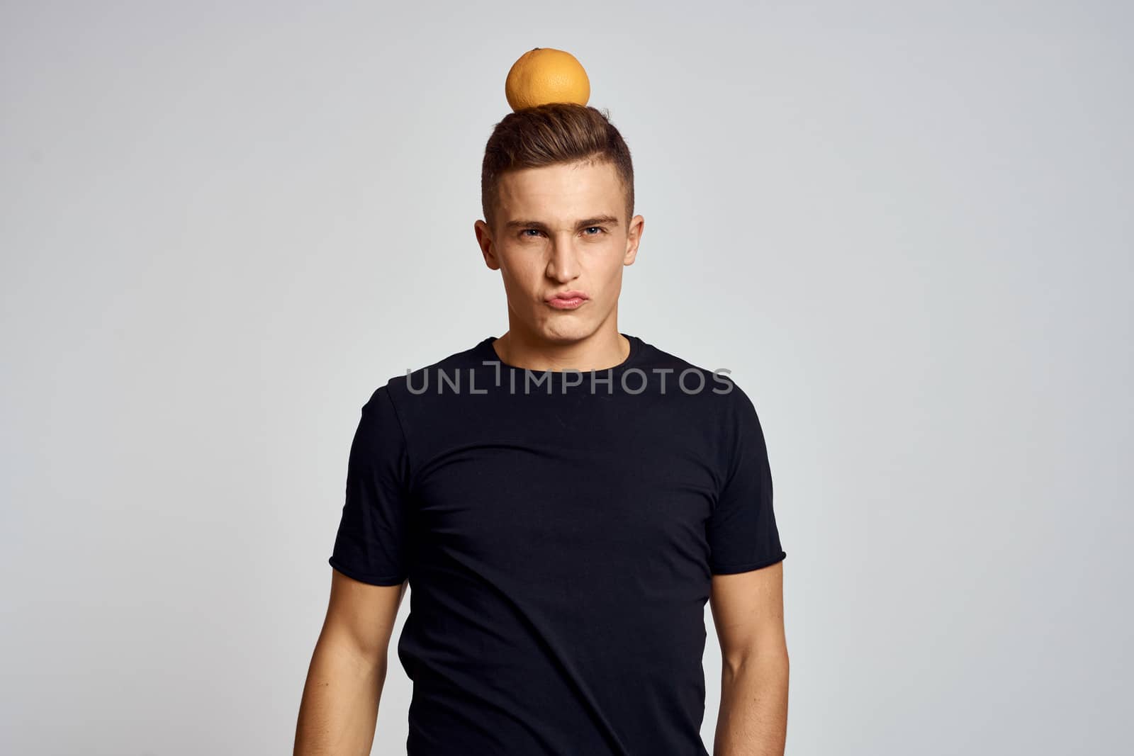 A guy with an orange in his hand and in a black T-shirt on a light background cropped view by SHOTPRIME