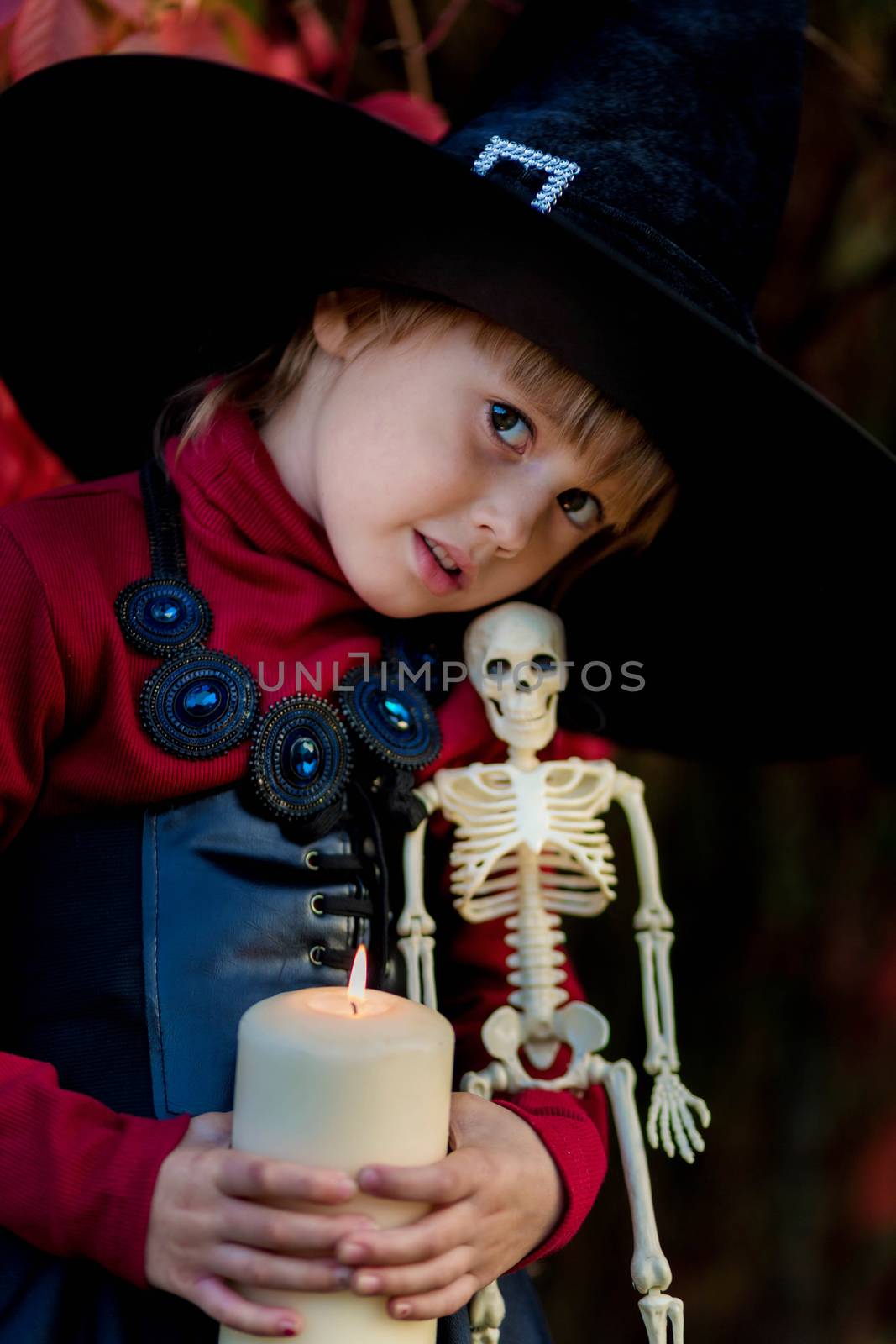 Little girl in a witch costume holding a skeleton on a halloween party in the garden