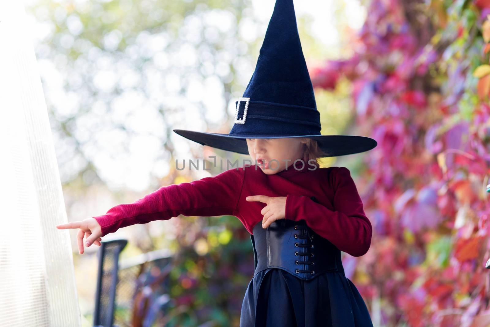 Little girl in witch costume posing on halloween party in the garden.