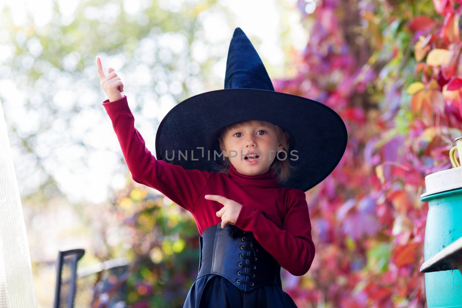 Little girl in witch costume posing on halloween party in the garden.