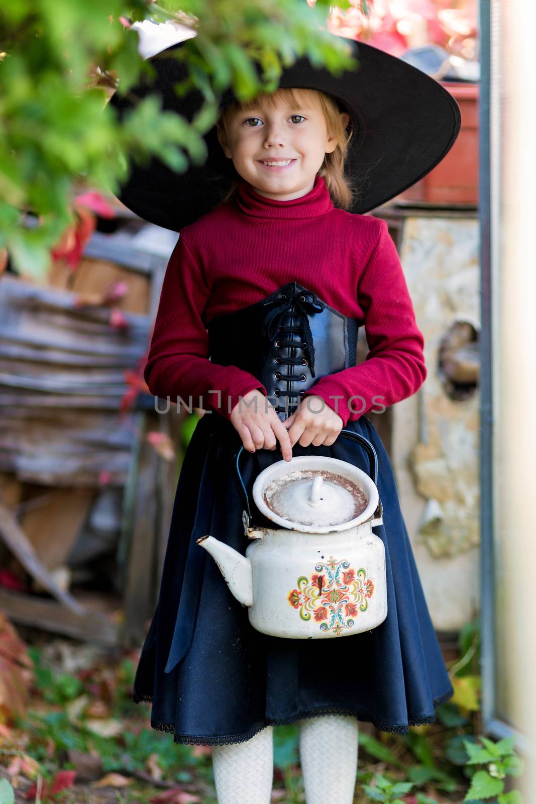 Little girl dressed as a witch holding a kettle on halloween party in the garden