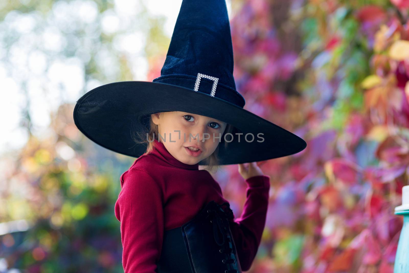 Little girl in witch costume making different faces on halloween party in the garden