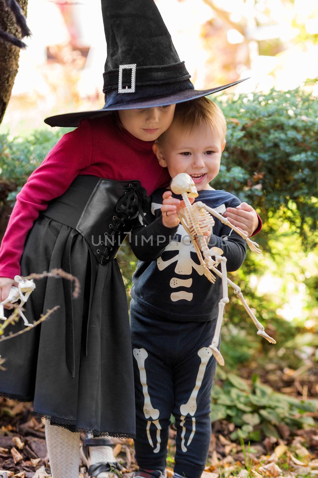 Little girl in witch costume and boy in skeleton costume on halloween party in the garden
