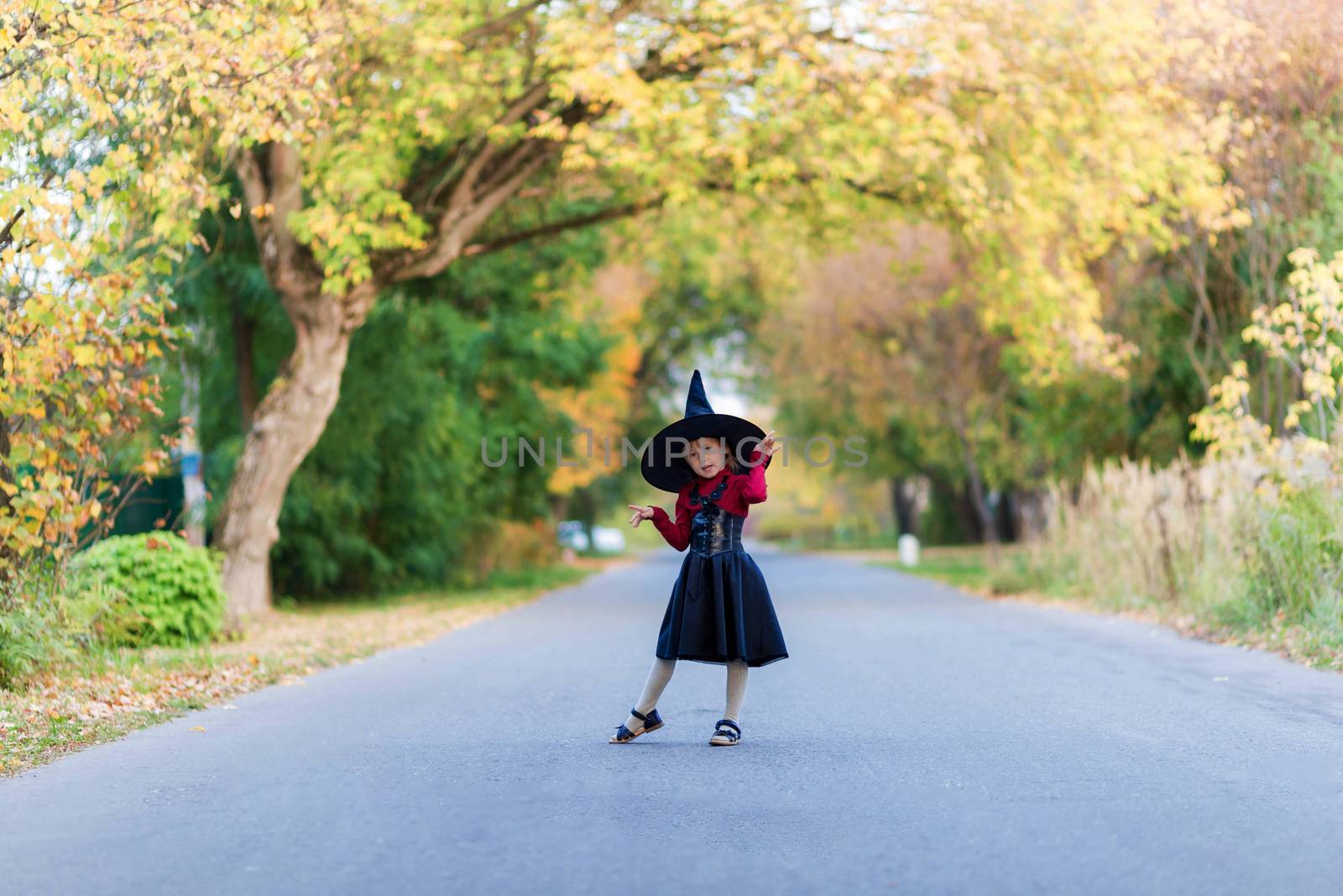 Little girl in a witch costume stands on the road on a halloween party in the village