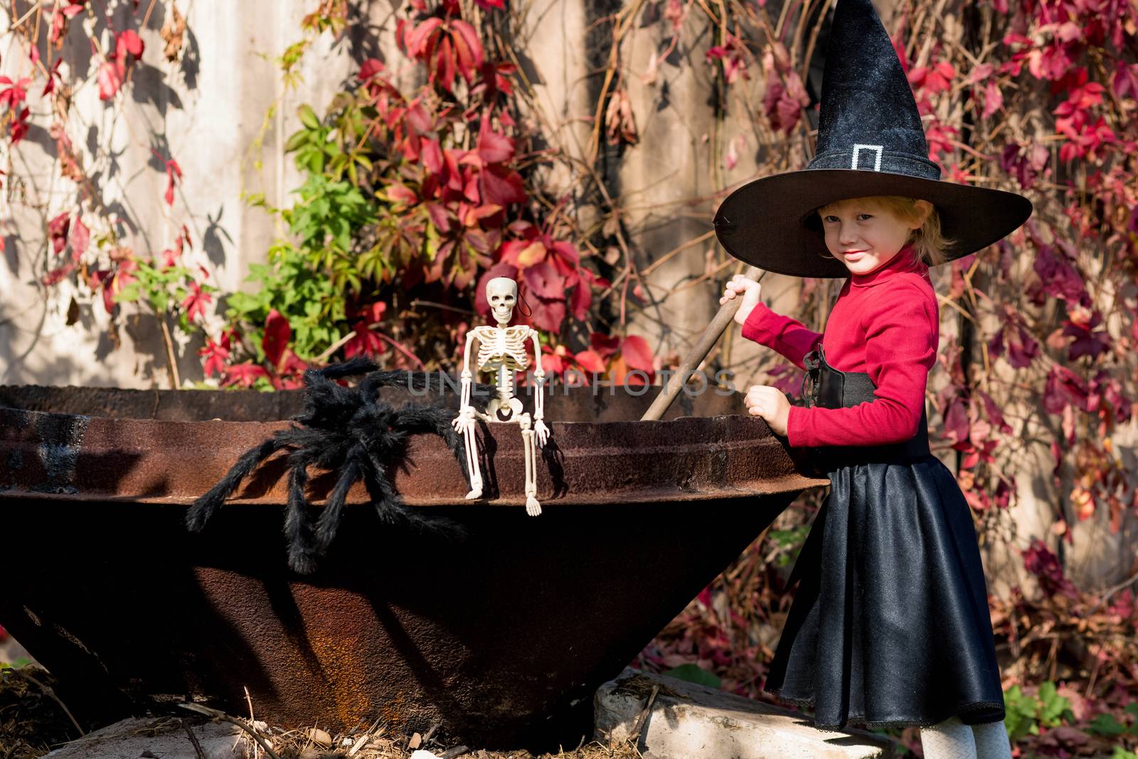 Little girl in a witch costume interferes with a potion on a halloween party in the garden