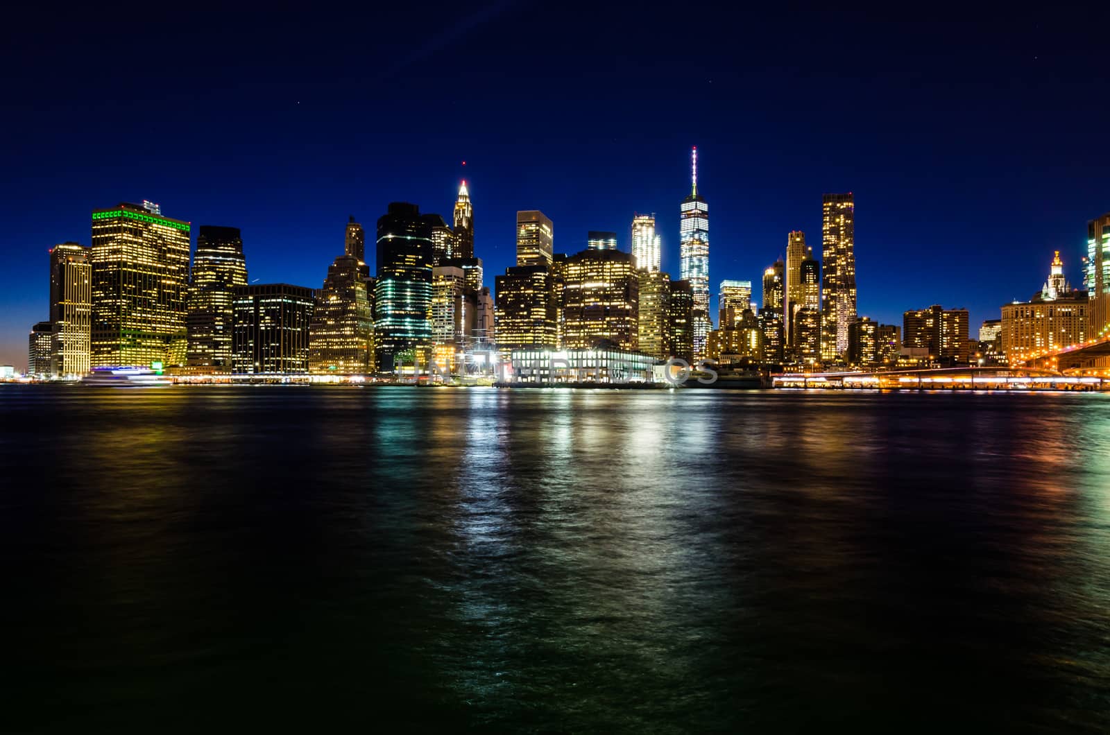 View of illuminated Manhattan skyline at twilight, with skyscraper lights reflected on the river. New York City, USA