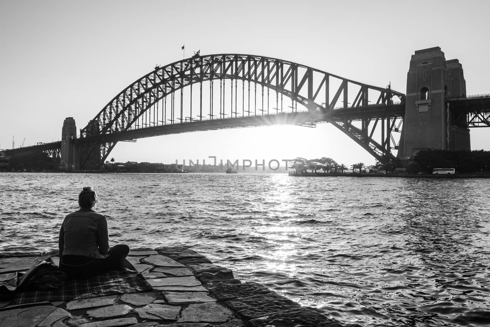 A lady contemplating from Kirribilli point the sun setting behind Harbour bridge. Black and white