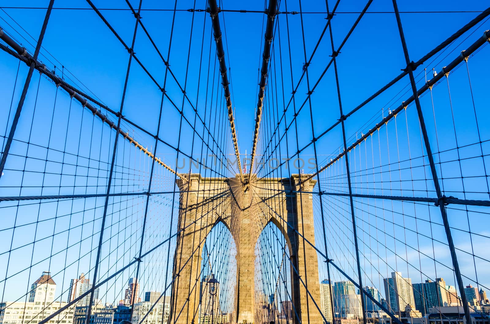 Low angle view of the web of cables of Brooklyn bridge in a sunny afternoon on a blue sky as background