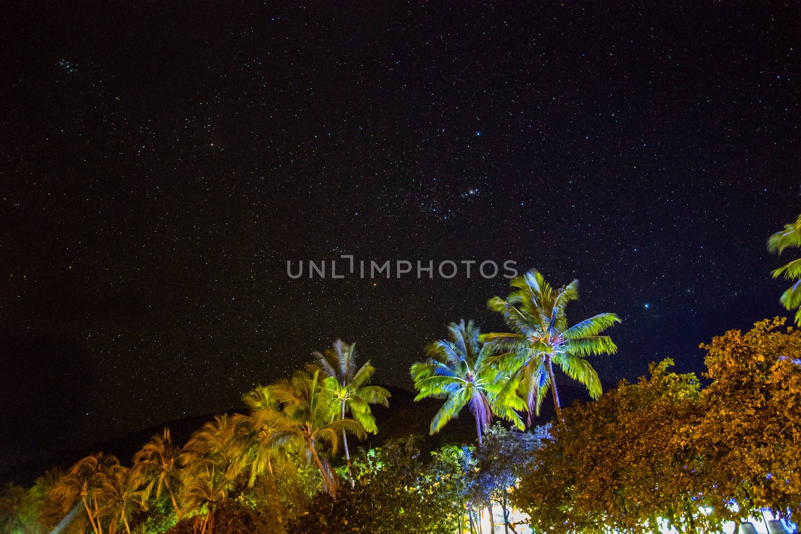 Starry night sky from Fitzroy Island beach illuminated by the resort colourful lights. Queensland, Australia. 