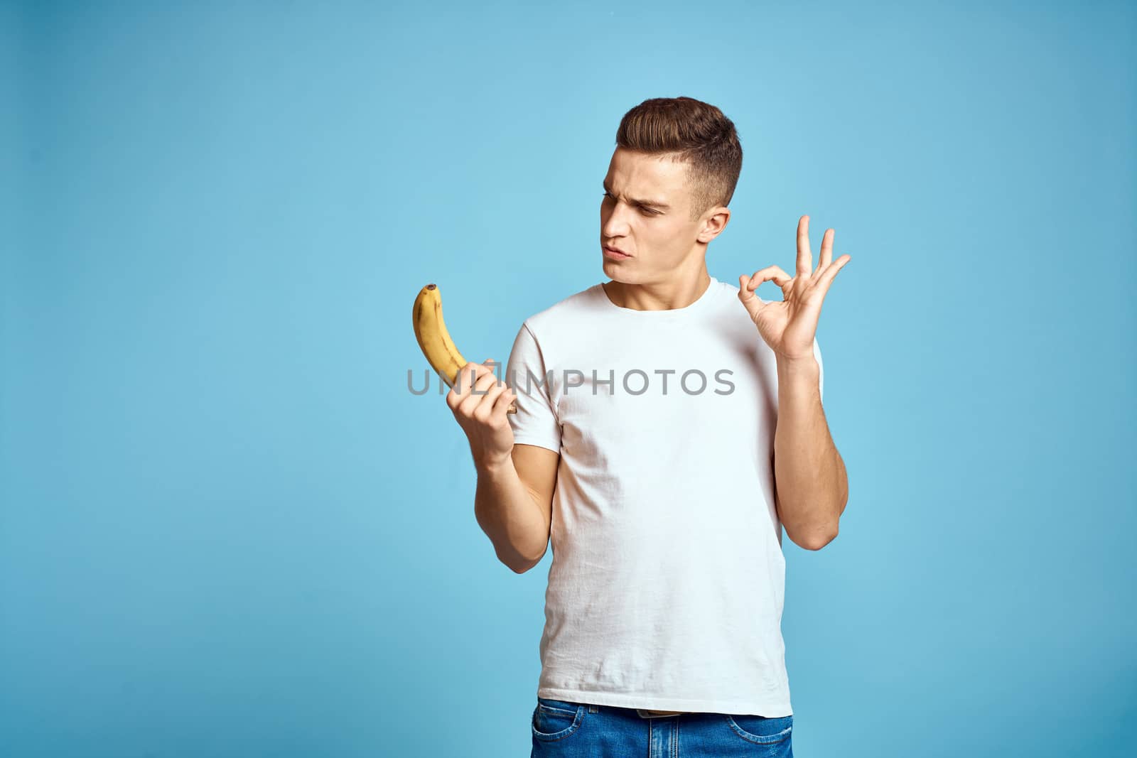 Happy man with fresh fruits gesturing with hands blue background white t-shirt vitamins bananas by SHOTPRIME